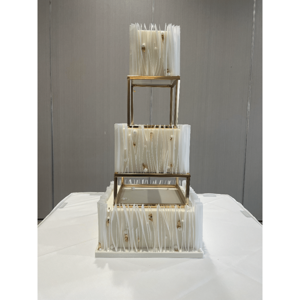 Elegant three-tier white cake with gold accents and decorative details on a table.