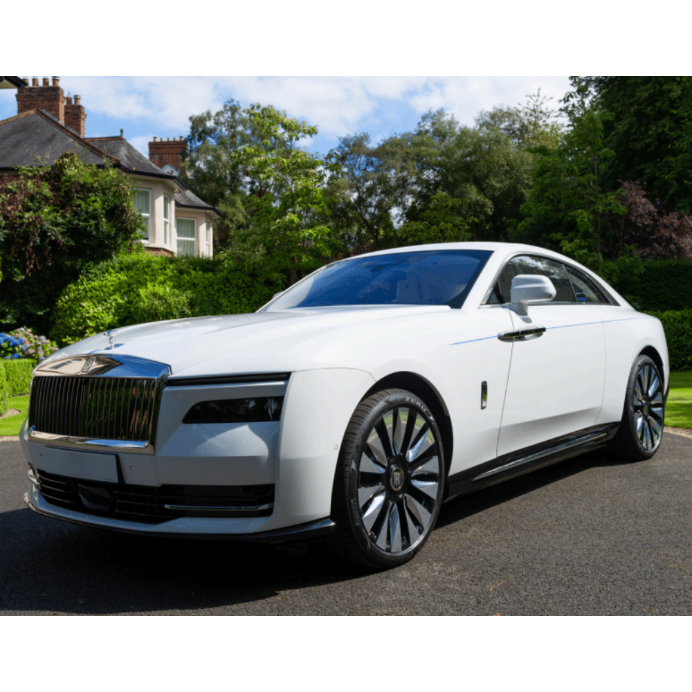 White luxury car parked on driveway with greenery and house in the background.