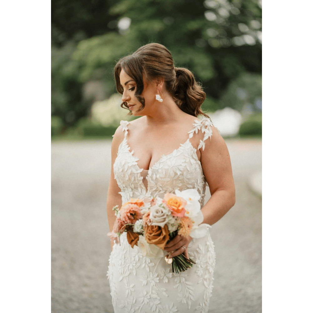 Bride holding a floral bouquet in a detailed lace wedding dress outdoors.