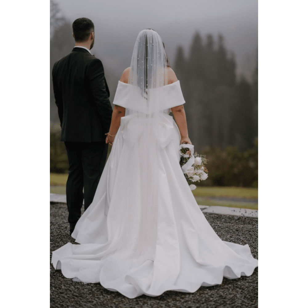 Bride and groom holding hands outdoors, wearing wedding attire, with a scenic misty background.