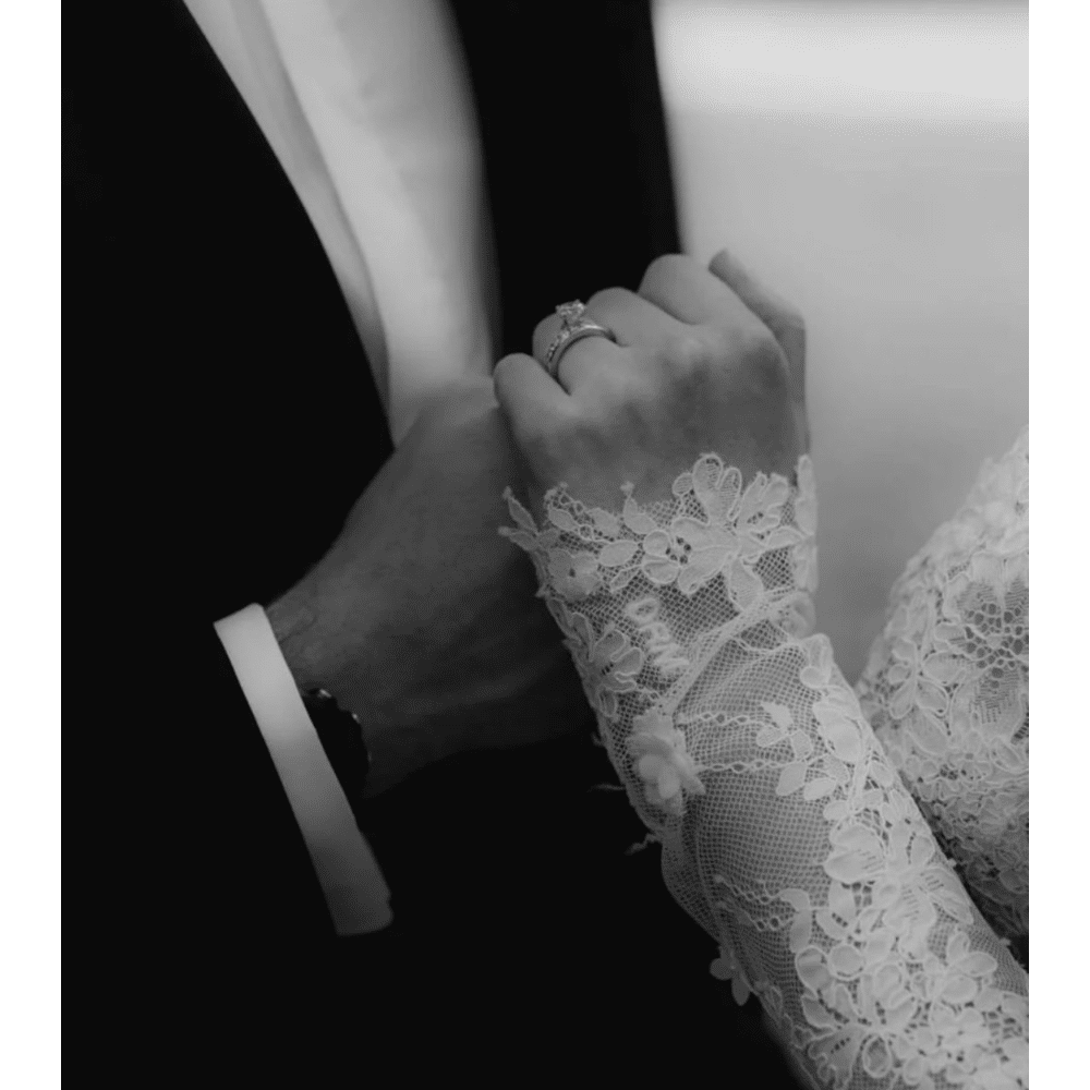 Bride and groom holding hands, showing lace sleeve and wedding ring.