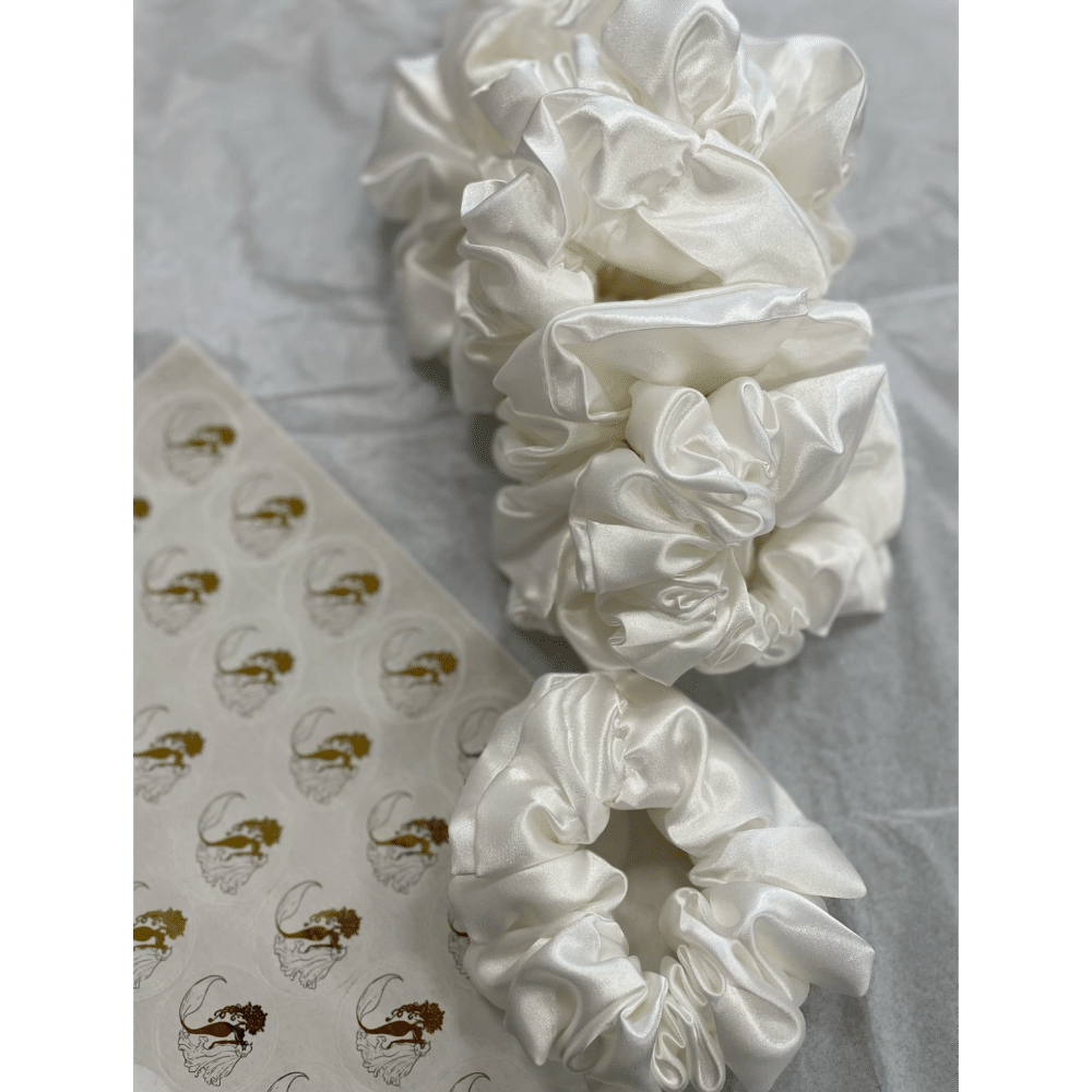 Silk scrunchies on a textured surface with logo stickers nearby.