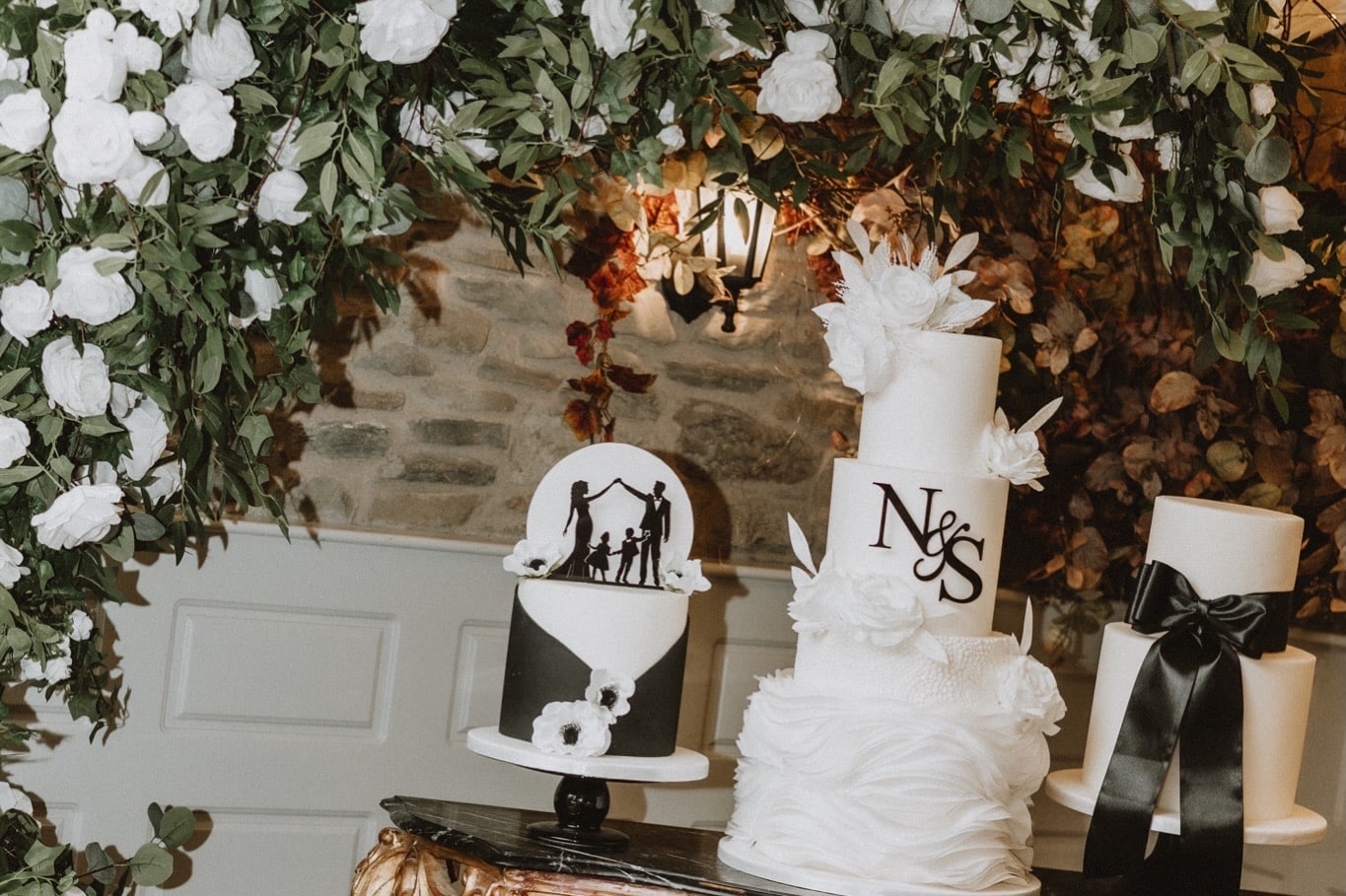 Elegant wedding cake display at Darver Castle featuring three bespoke black and white cakes by Claire Press Cakes beneath a floral arch at Natalie and Stephen’s wedding