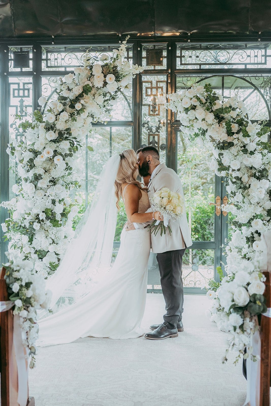 Newlyweds first kiss under stunning white floral pillars at wedding ceremony at The Old Rectory, Killyman, Northern Ireland