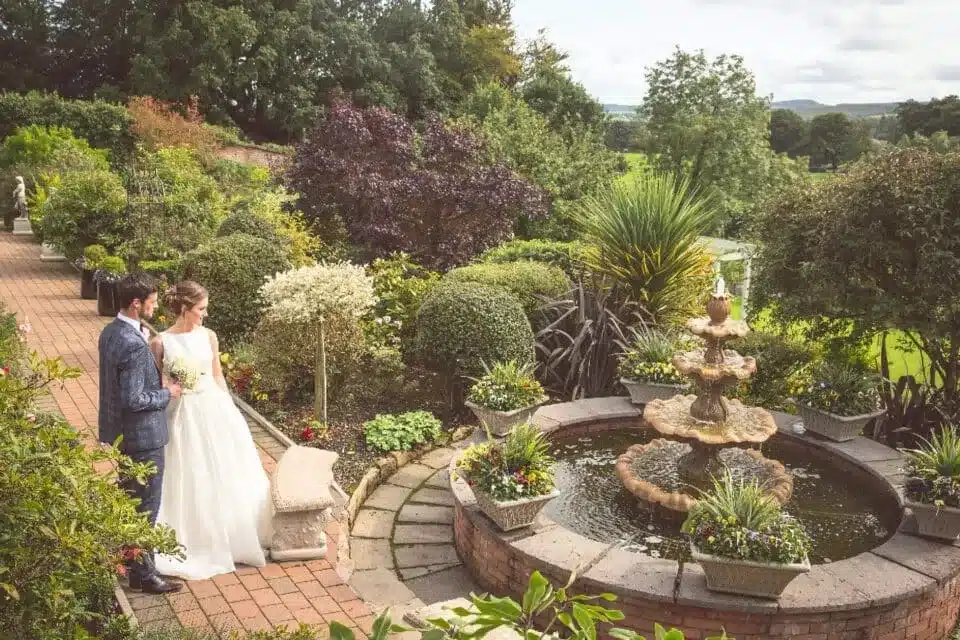Garden wedding venue with fountain and couple walking, featured in vendor listing card.