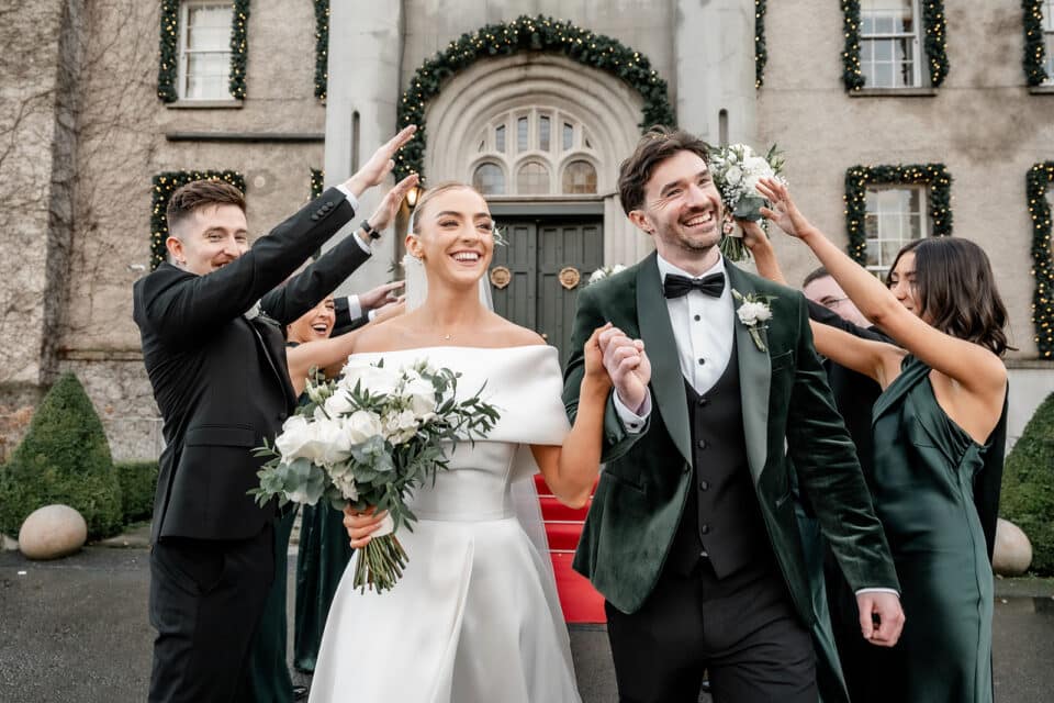 Wedding couple with bridal party celebrating outside a decorated castle entrance.
