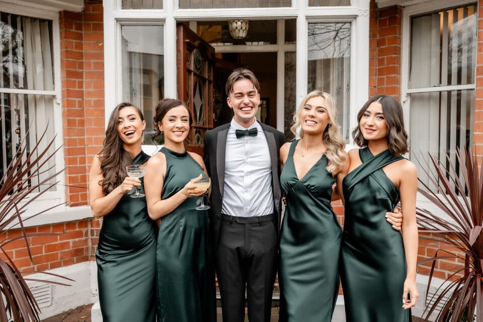 Five people in formal attire smiling and posing outside a brick building.