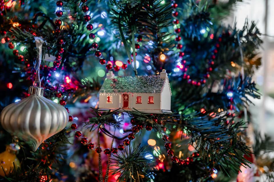 Christmas tree with a house ornament, red beads, and colorful lights.