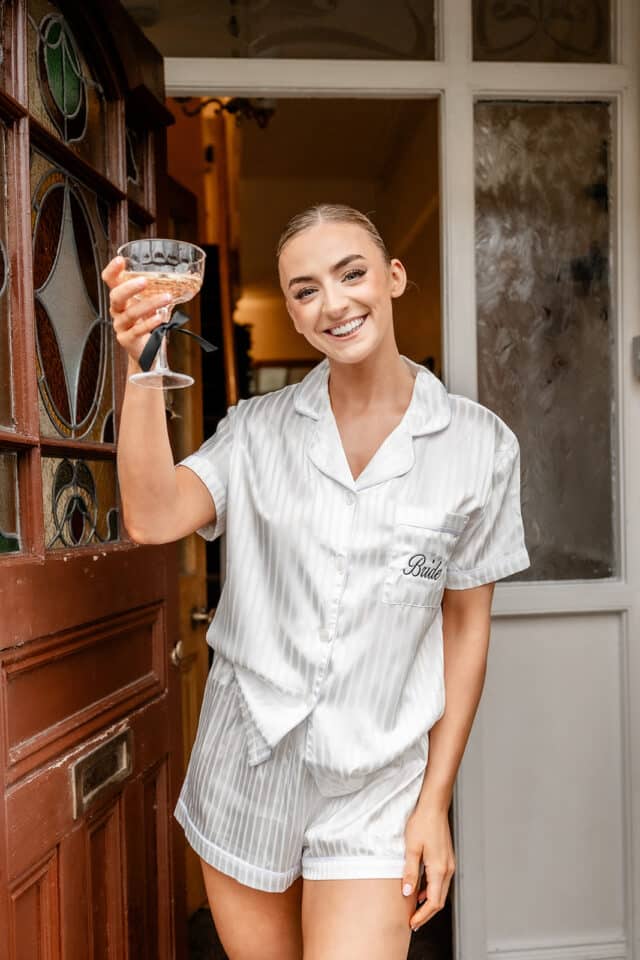 Bride in striped pajamas holding a champagne glass, smiling at the camera.