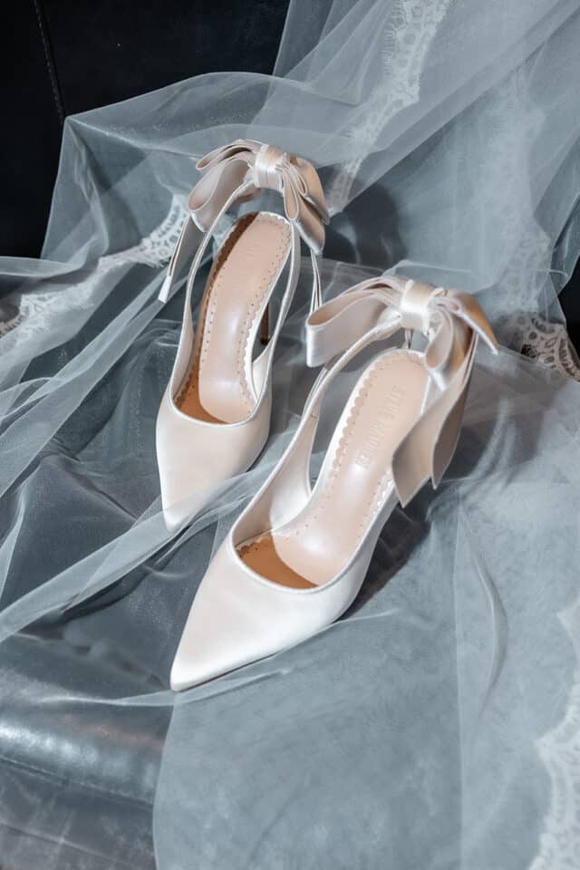 Elegant white high-heeled shoes with bows on lace fabric.