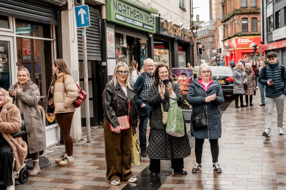 People gathered on a city street clapping outside shops, including Northern Vape.