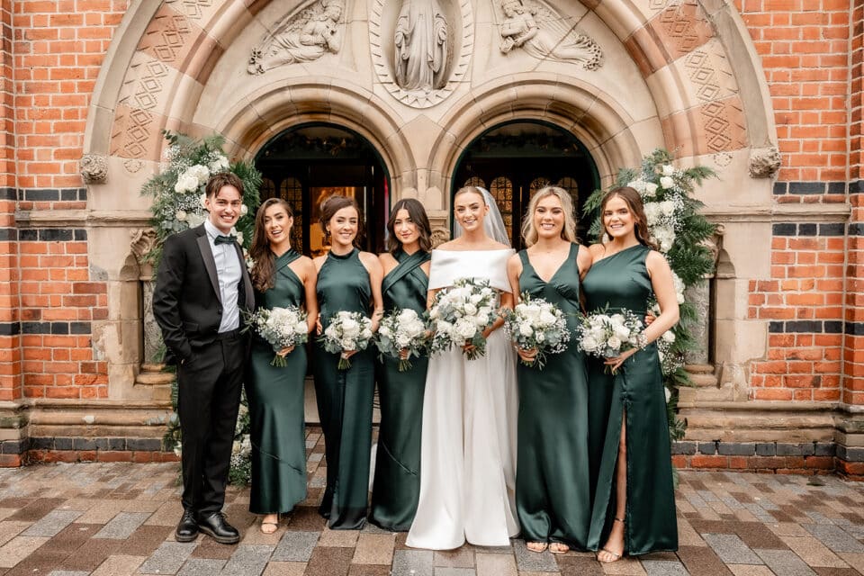 Bride and bridal party in green dresses and suits at Bellingham Castle entrance.