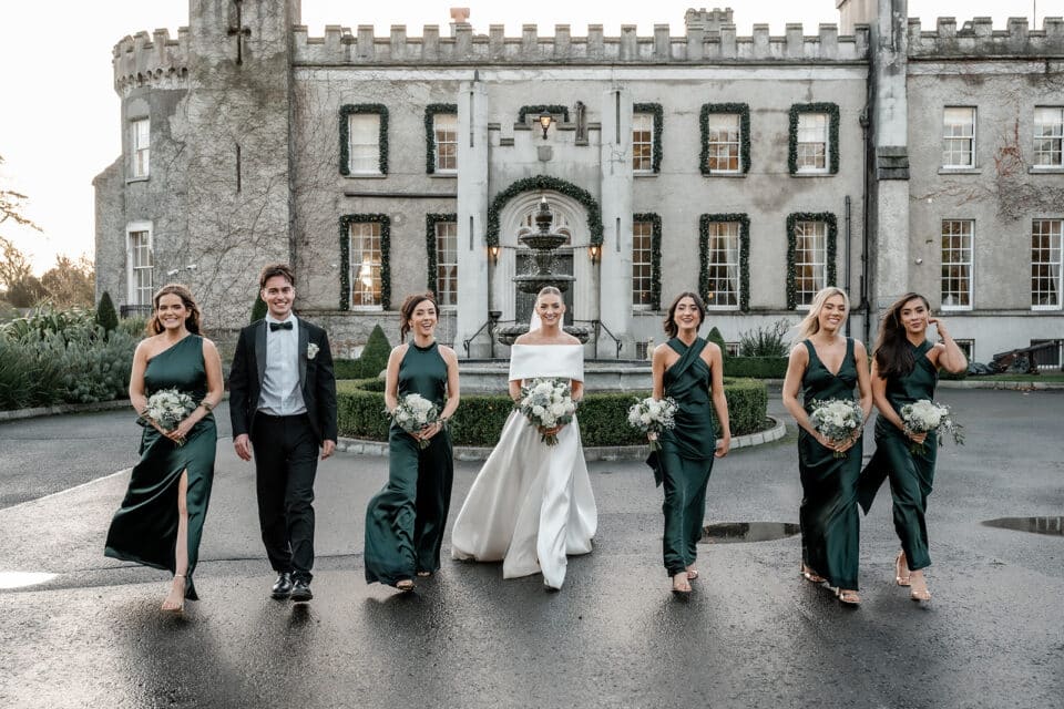 Bride and bridesmaids in green dresses with a groomsman walking outside Bellingham Castle.