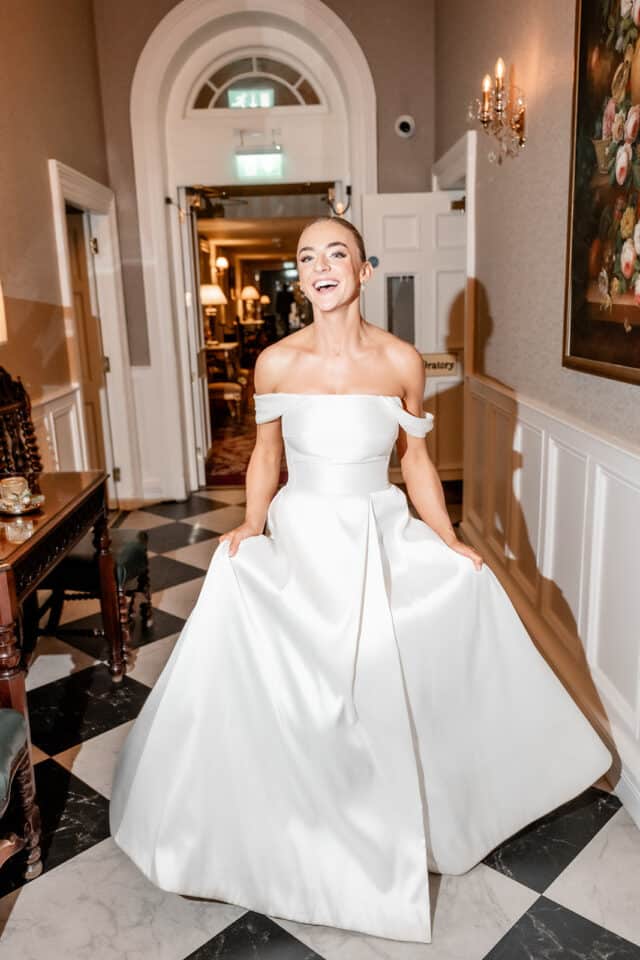 Bride in elegant white gown smiling indoors at Bellingham Castle.