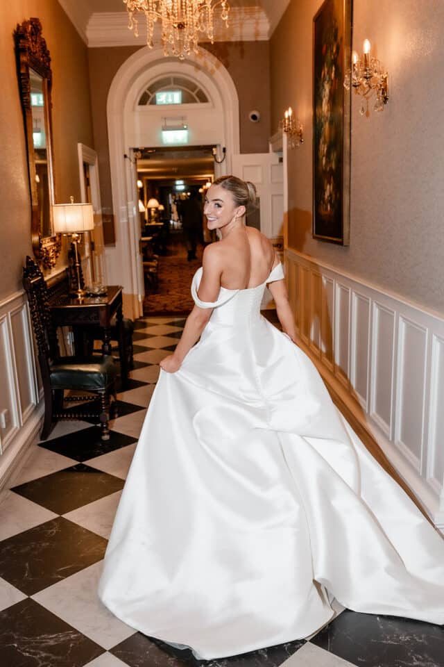 Bride in white gown smiling in an elegant hallway at Bellingham Castle.