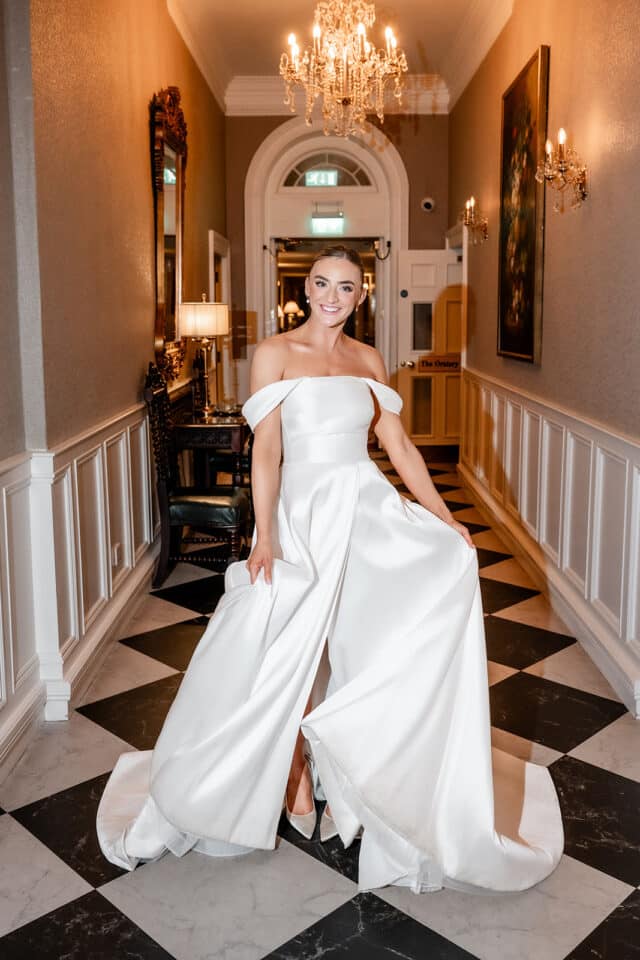 Bride in a white wedding dress smiling in a castle hallway with chandeliers.