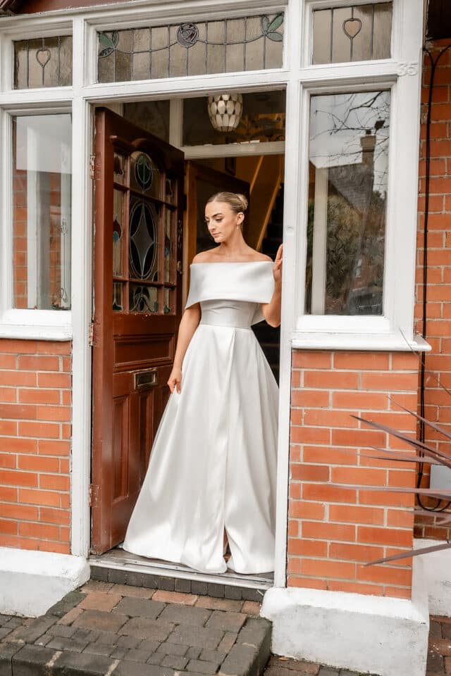 Bride in elegant white gown standing in a doorway with stained glass panels.