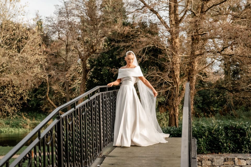 Bride in elegant white gown and veil posing on a bridge at Bellingham Castle.