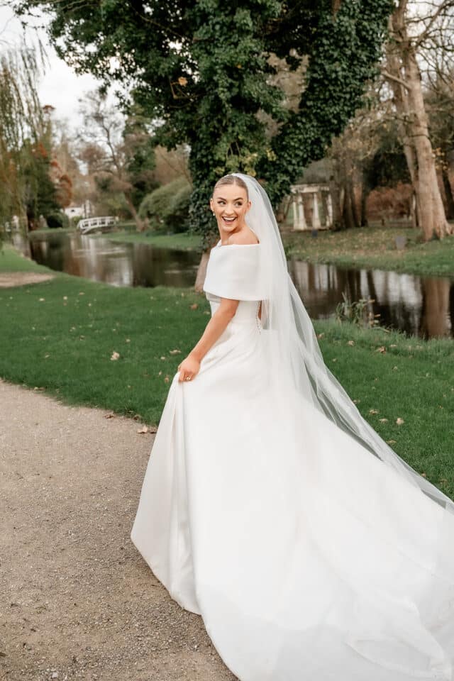 Bride in elegant white dress and veil smiling at Bellingham Castle garden.