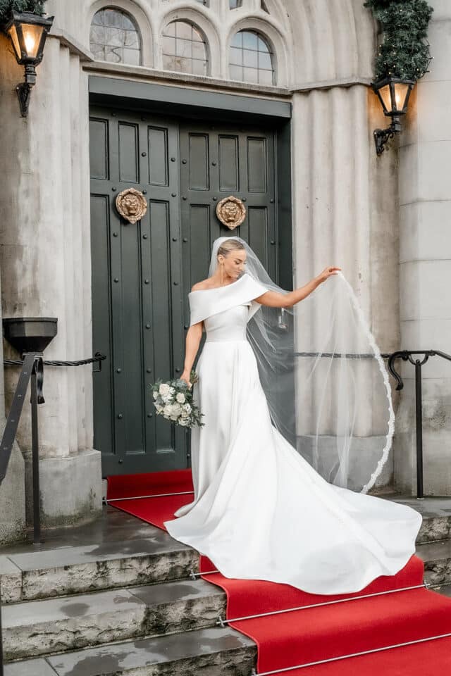 Bride in elegant white gown on red carpet outside Bellingham Castle door.