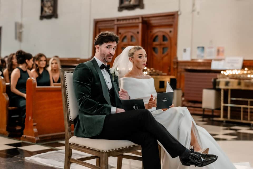 Bride and groom seated in a church, holding booklets, during their wedding ceremony.