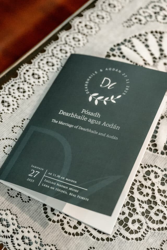 Wedding program for Dearbhaile and Aodhàn at Bellingham Castle, November 27, 2025, on a lace tablecloth.