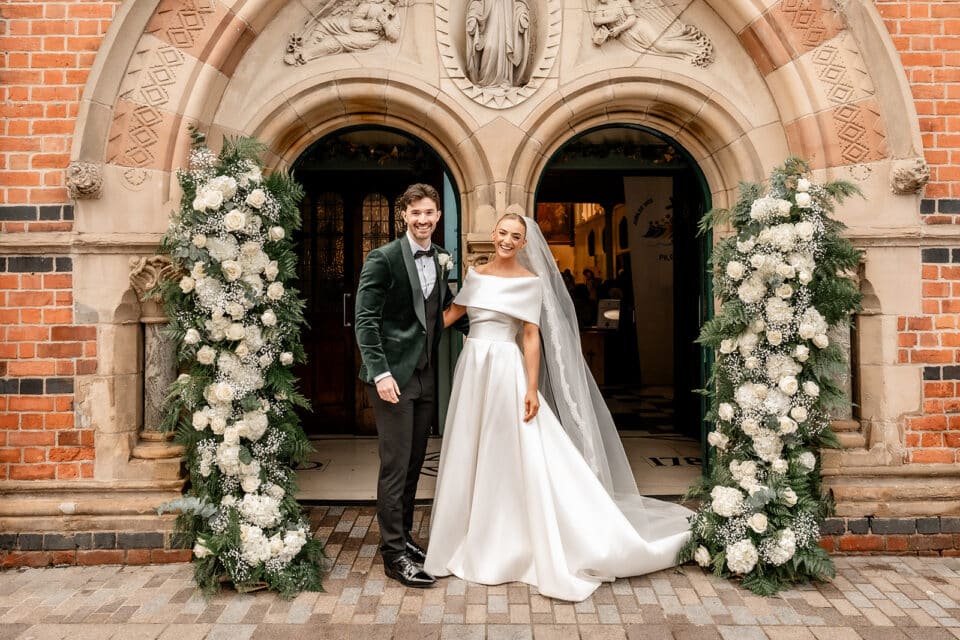 Bride and groom standing at ornate entrance with floral decorations at Bellingham Castle.
