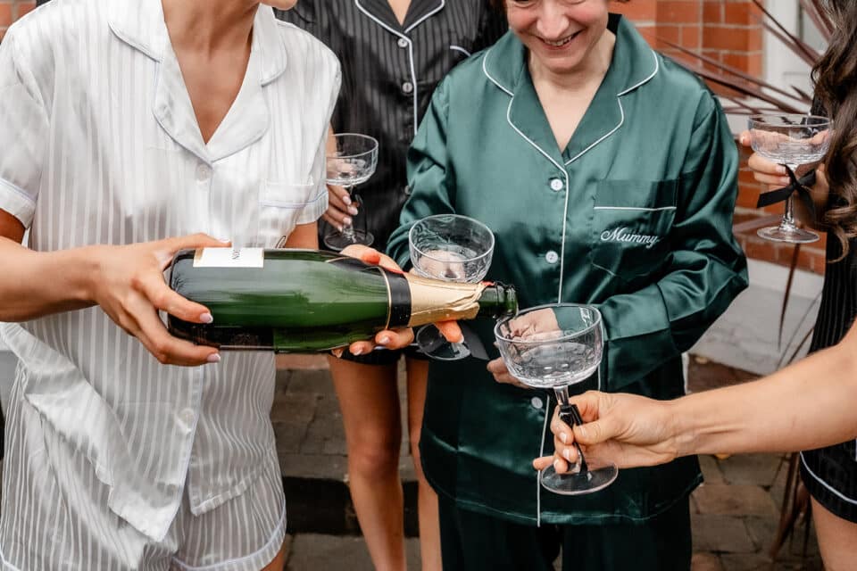 Women in pajamas pour champagne into glasses at a gathering.