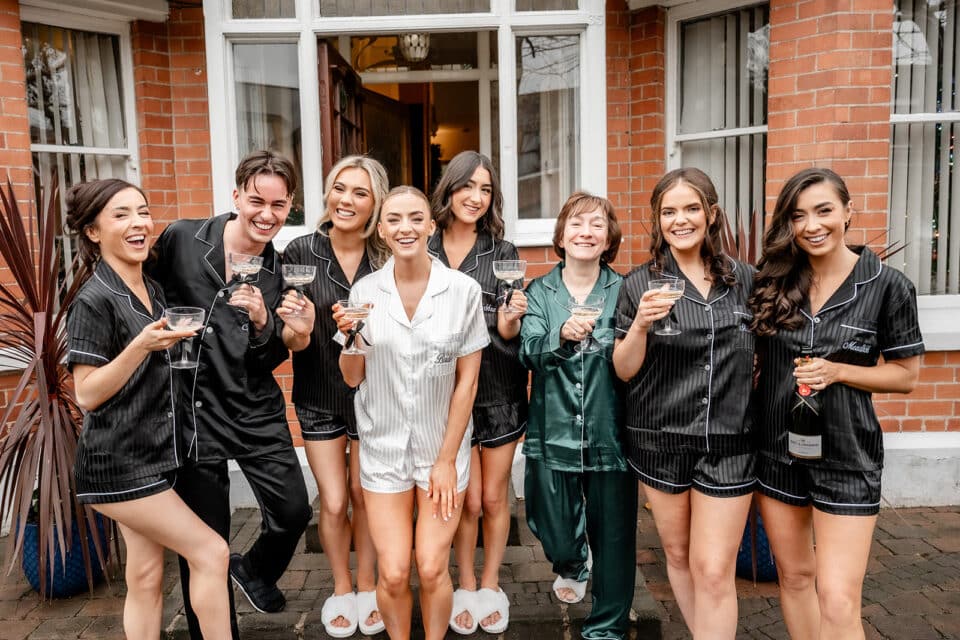 Group celebrating in matching pajamas with champagne outside brick building.