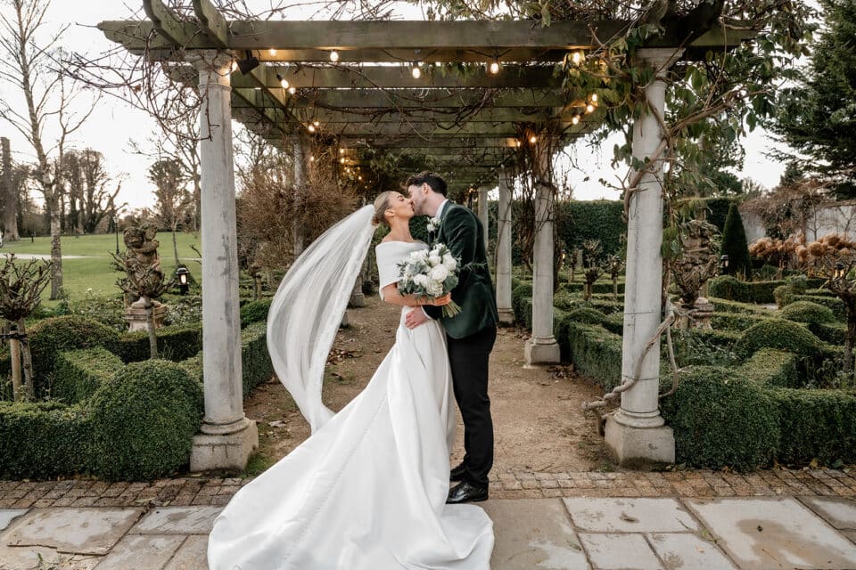 Bride and groom kissing under a garden pergola at Bellingham Castle.