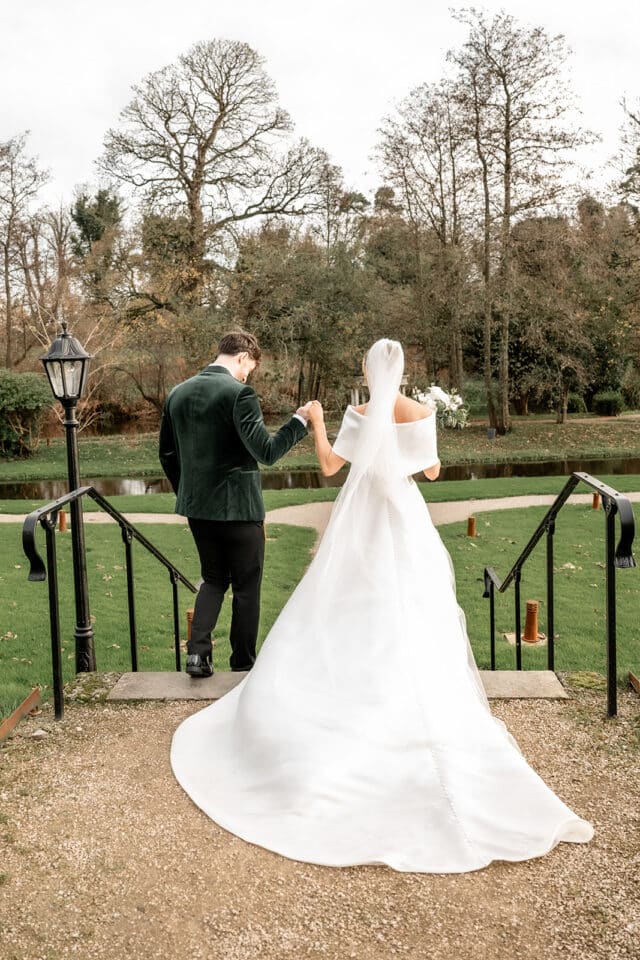 Bride and groom walking hand in hand at Bellingham Castle with scenic background.