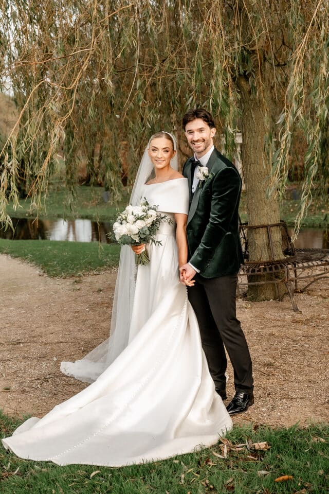 Bride and groom posing outdoors in elegant attire at Bellingham Castle.