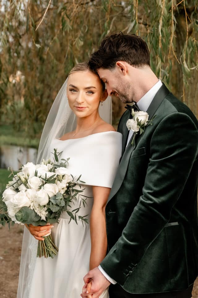 Bride and groom posing romantically outdoors with white roses at Bellingham Castle.