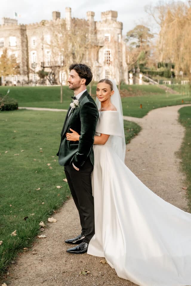 Bride and groom posing on a path with Bellingham Castle in the background.