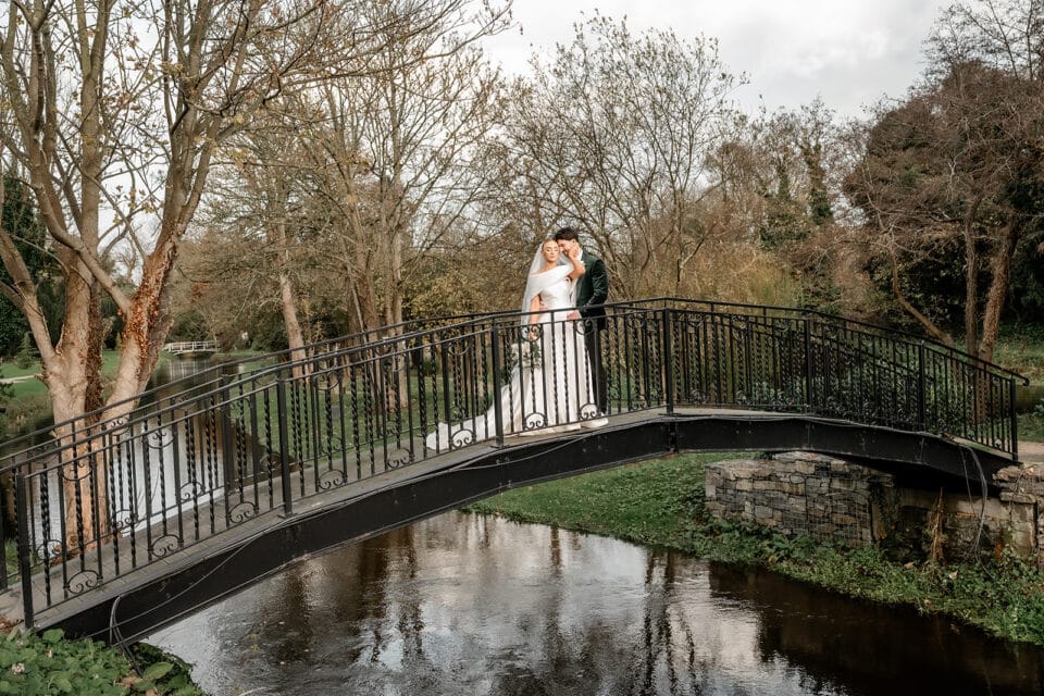 Bride and groom embracing on a scenic bridge at Bellingham Castle.