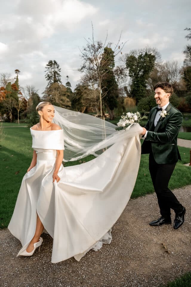 Bride and groom joyfully walking outside, bride's veil flowing, at Bellingham Castle wedding.