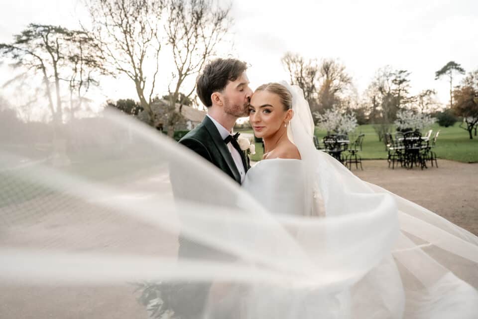 Bride and groom embrace outdoors with flowing veil at Bellingham Castle.