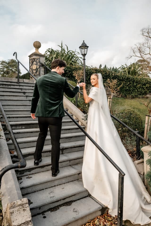 Bride and groom holding hands on stone stairs at Bellingham Castle.