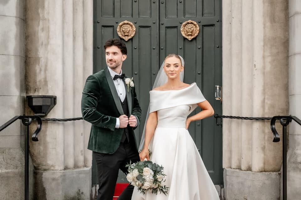 Bride and groom posing in formal attire outside Bellingham Castle.