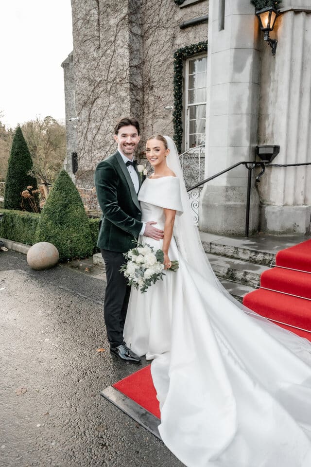 Bride and groom pose in wedding attire at Bellingham Castle entrance.