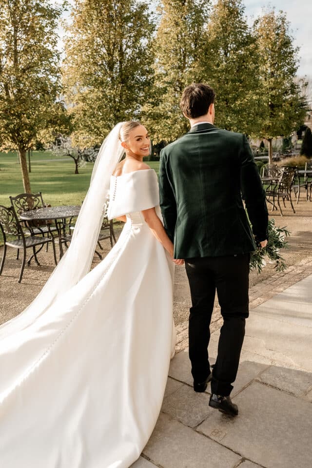 Bride and groom walking outdoors at Bellingham Castle, bride in white gown with veil, groom in dark suit.