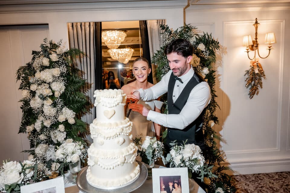Bride and groom cutting a tiered wedding cake surrounded by floral arrangements at Bellingham Castle.