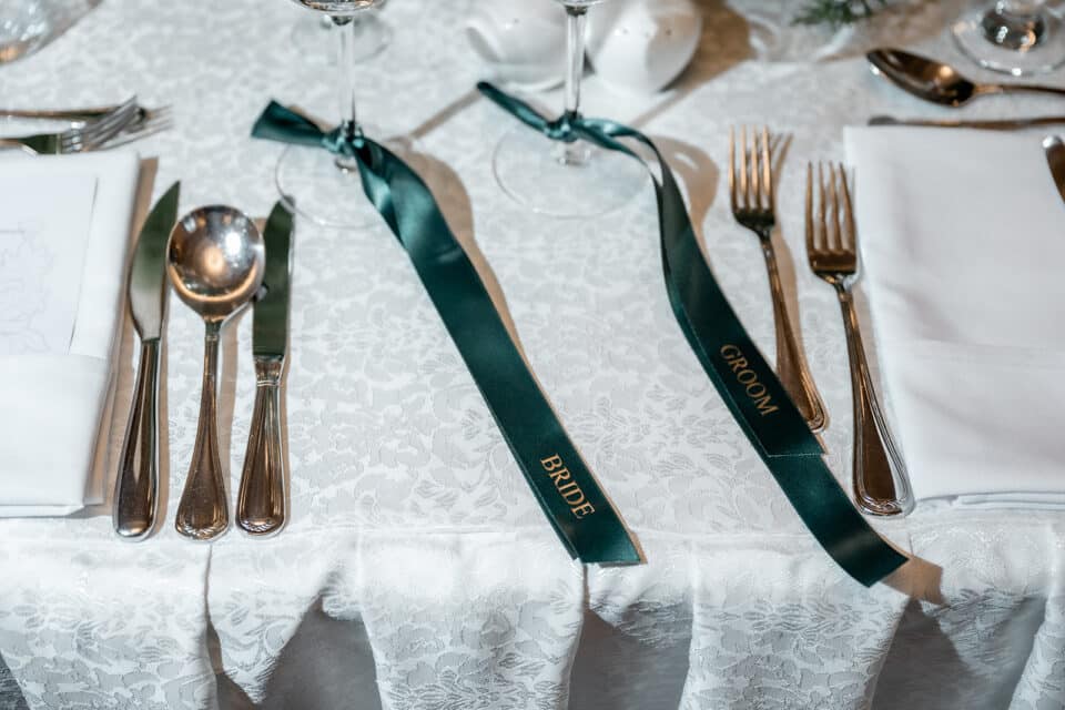 Wedding table setting with white tablecloth, silverware, and green ribbons labeled "Bride" and "Groom" at Bellingham Castle.