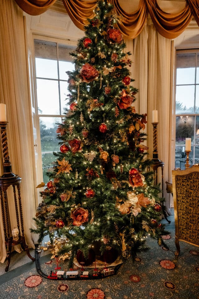 Elegant Christmas tree adorned with red and gold ornaments, surrounded by vintage decor at Bellingham Castle.