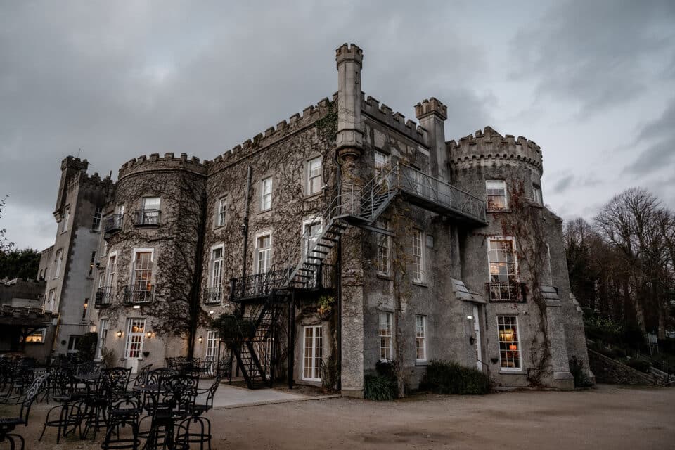 Historic Bellingham Castle exterior with ivy-covered walls and outdoor seating on a cloudy day.