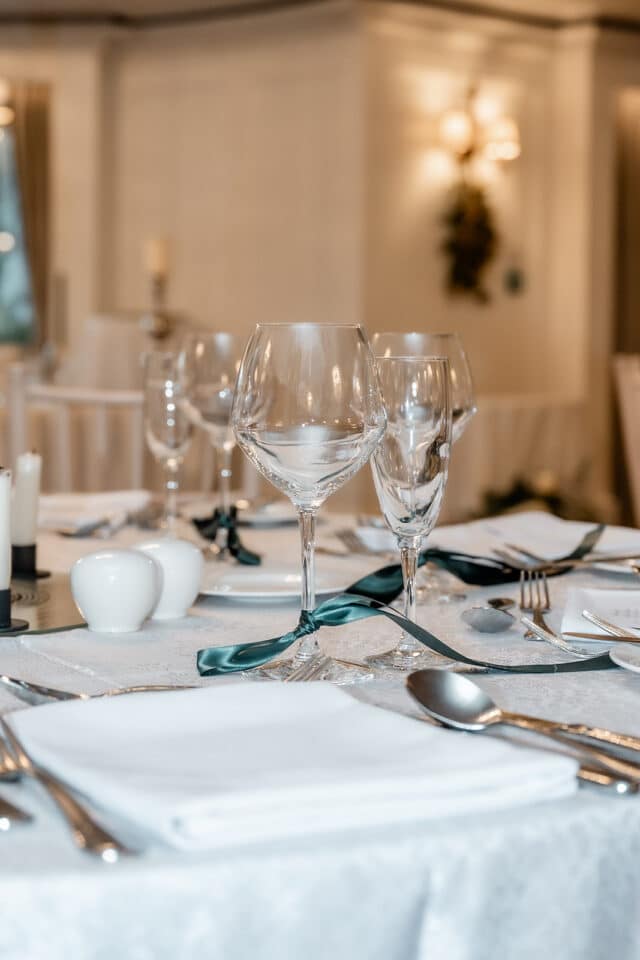 Elegant table setting with wine glasses and white linens, adorned with green ribbon, in a formal dining setting.