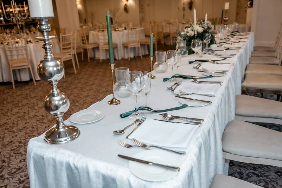 Elegant wedding table setting with white linens, green candles, floral centerpiece, and silver cutlery at Bellingham Castle.