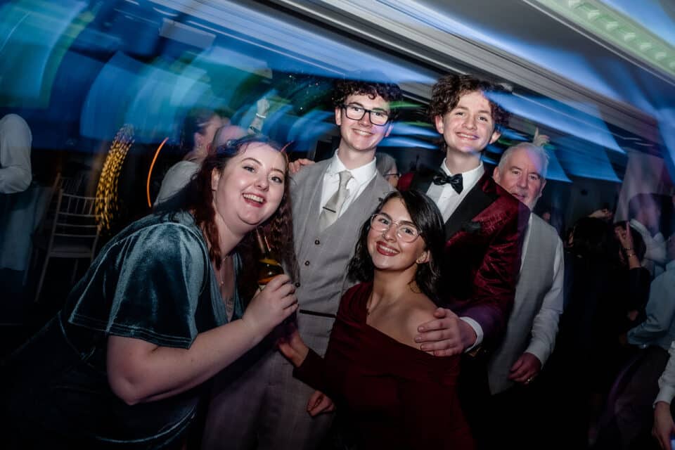 Group of people smiling and posing at an indoor event with colorful lighting effects.