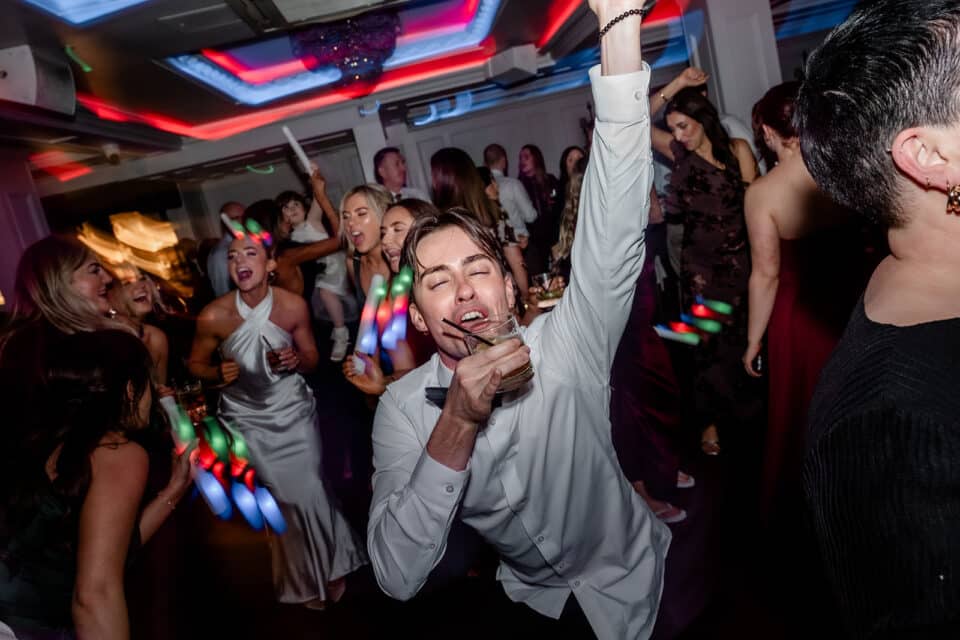 People dancing and celebrating energetically at a party with colorful lights.