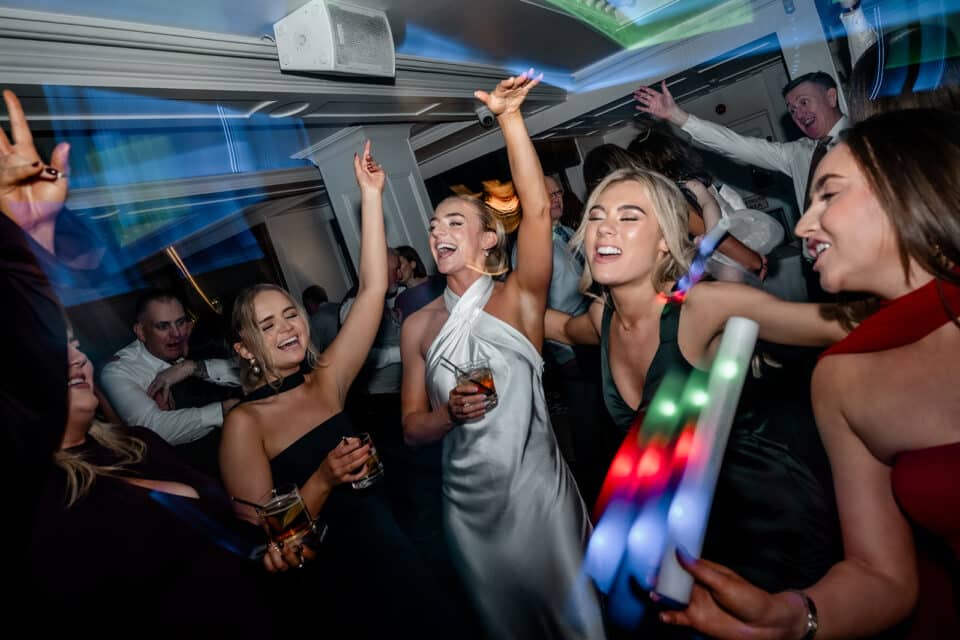 Guests dancing and celebrating at Bellingham Castle with drinks and colorful lights.